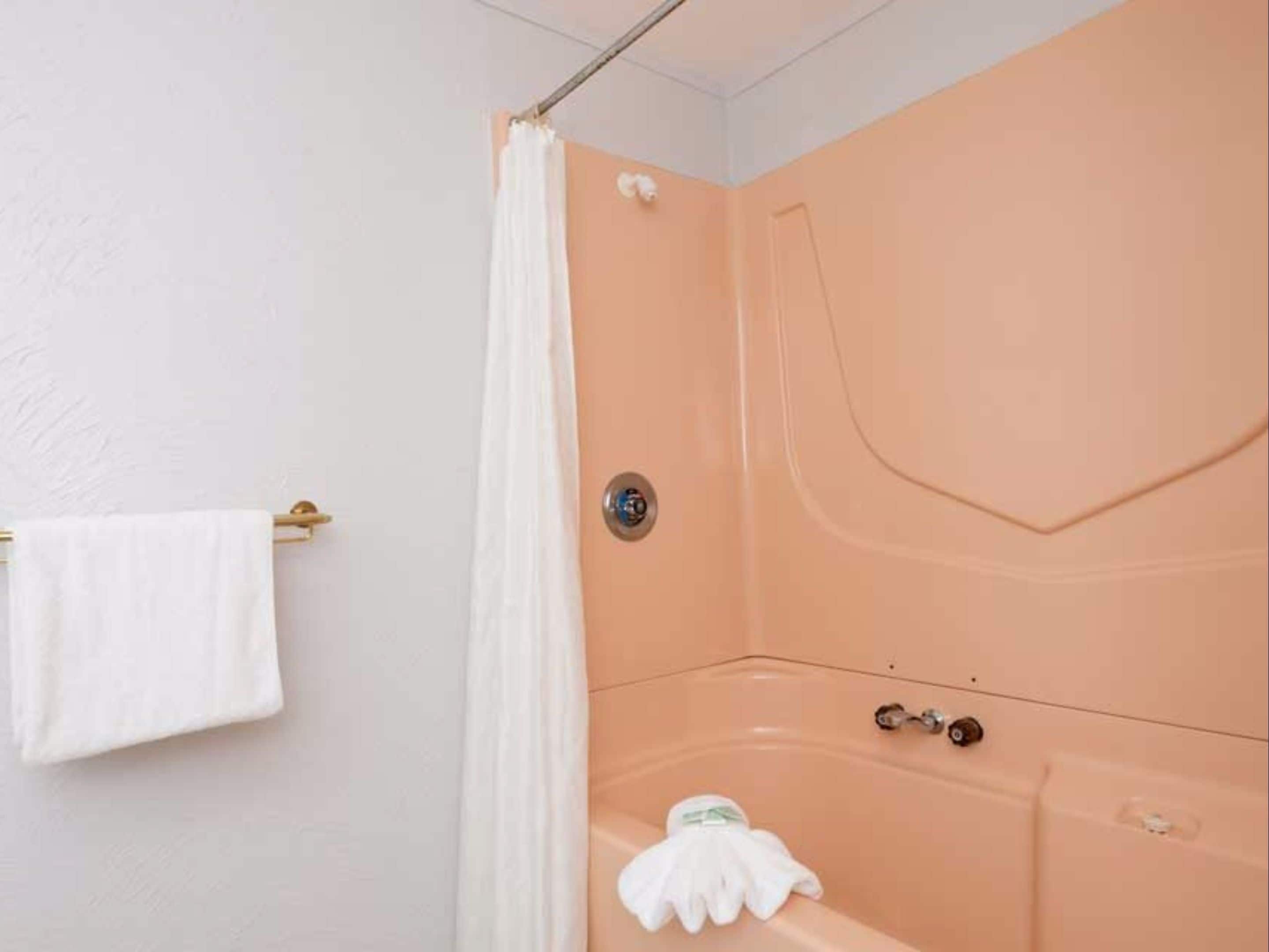 A bathroom with a peach-colored shower enclosure, a white towel on a rack, and a white bath mat on the floor.
