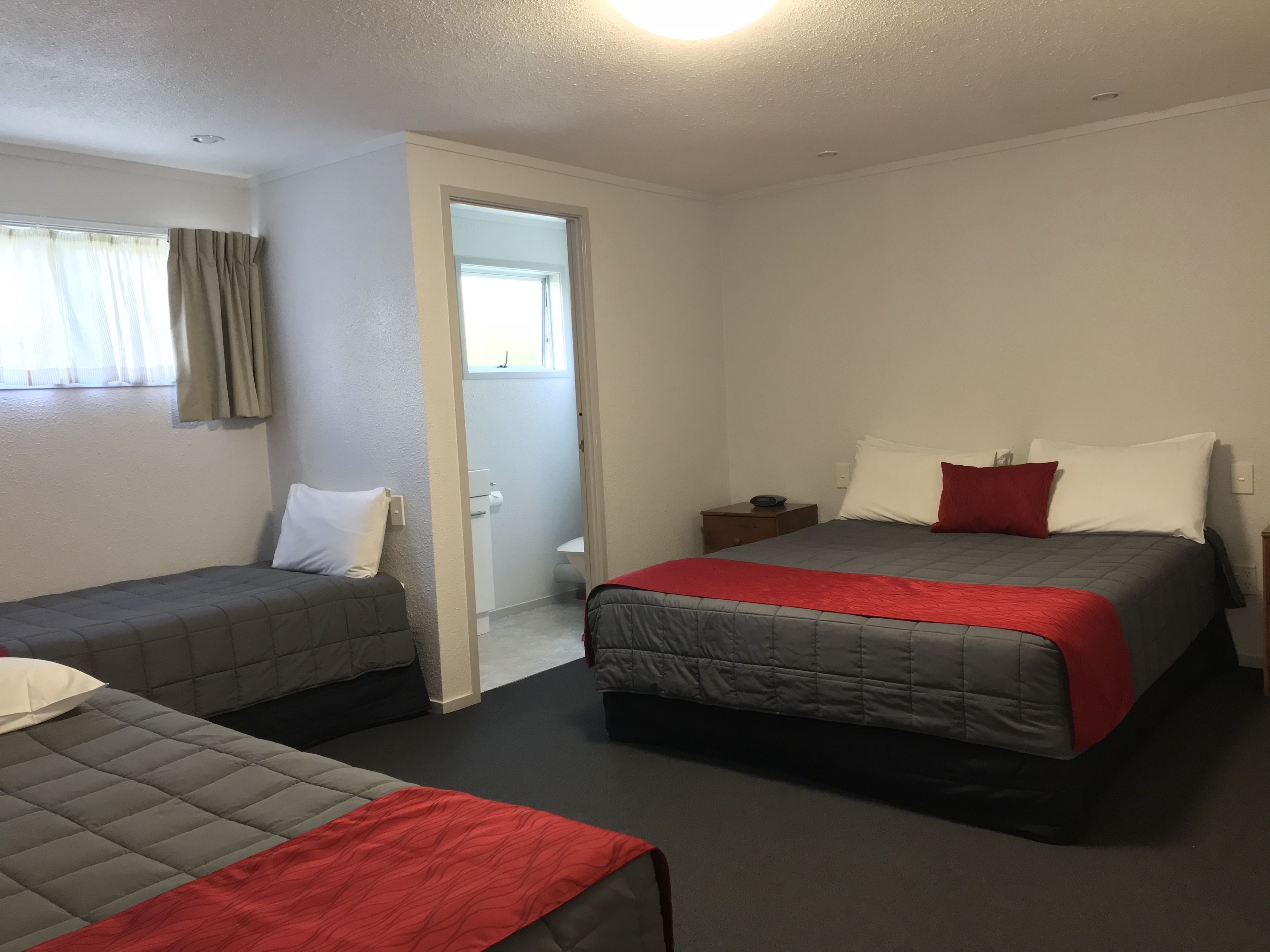 A hotel room with two single beds, a small bedside table with a lamp, and a door leading to a bathroom.