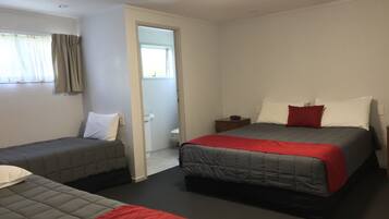 A hotel room with two single beds, a small bedside table with a lamp, and a door leading to a bathroom.