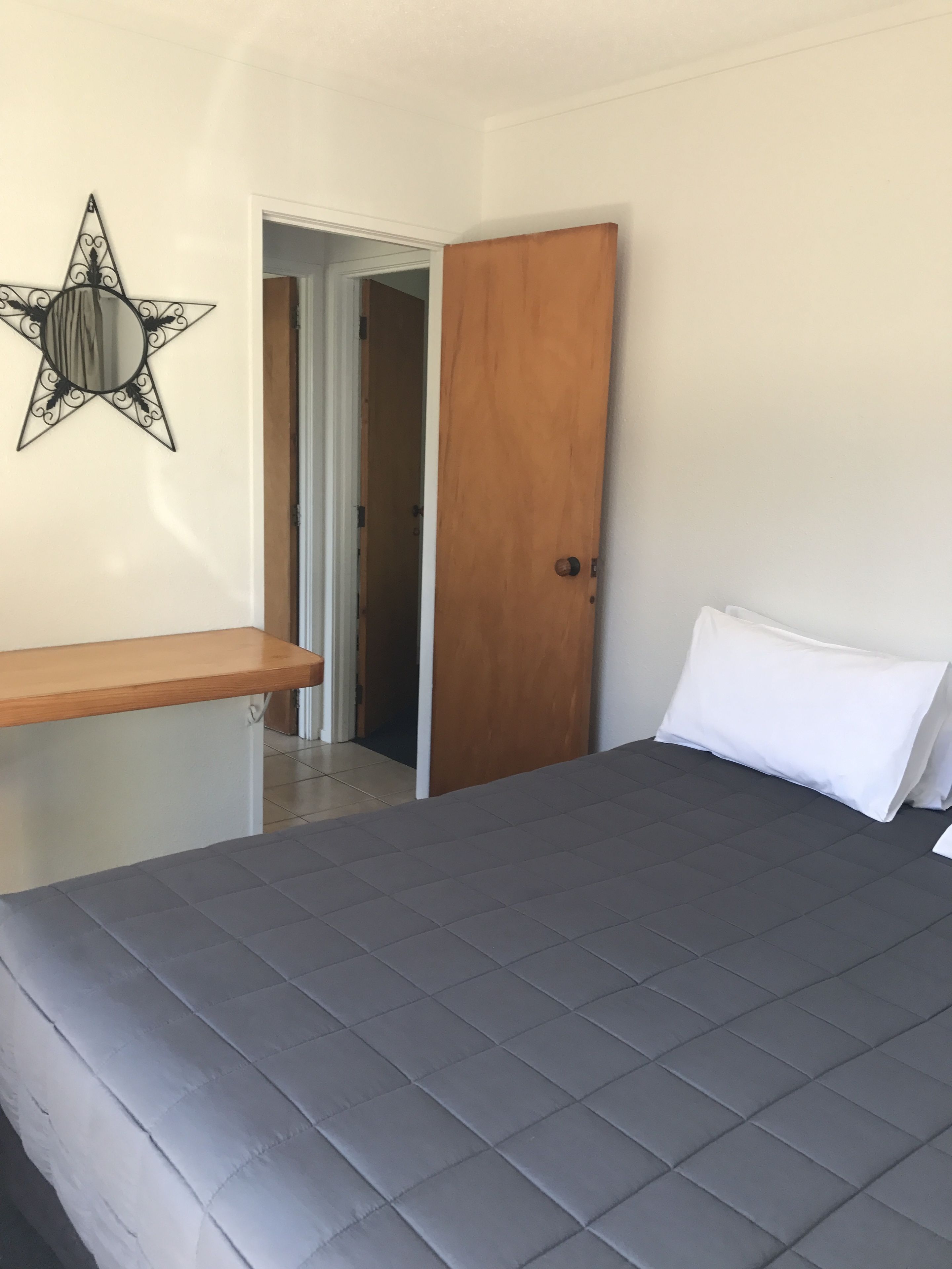 A bedroom with a bed, a wooden door, a star-shaped wall decoration, and a wooden shelf.
