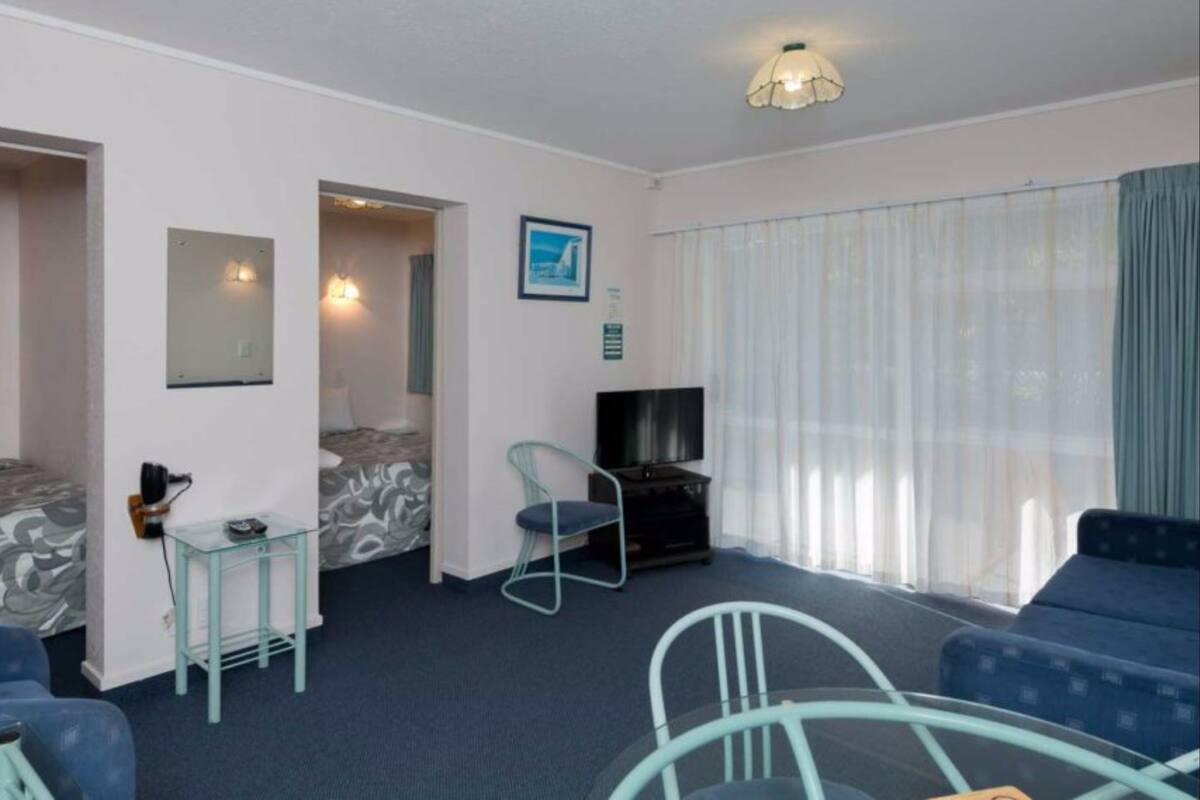 A hotel room with a bed, a TV, a small table, a chair, and a sofa.