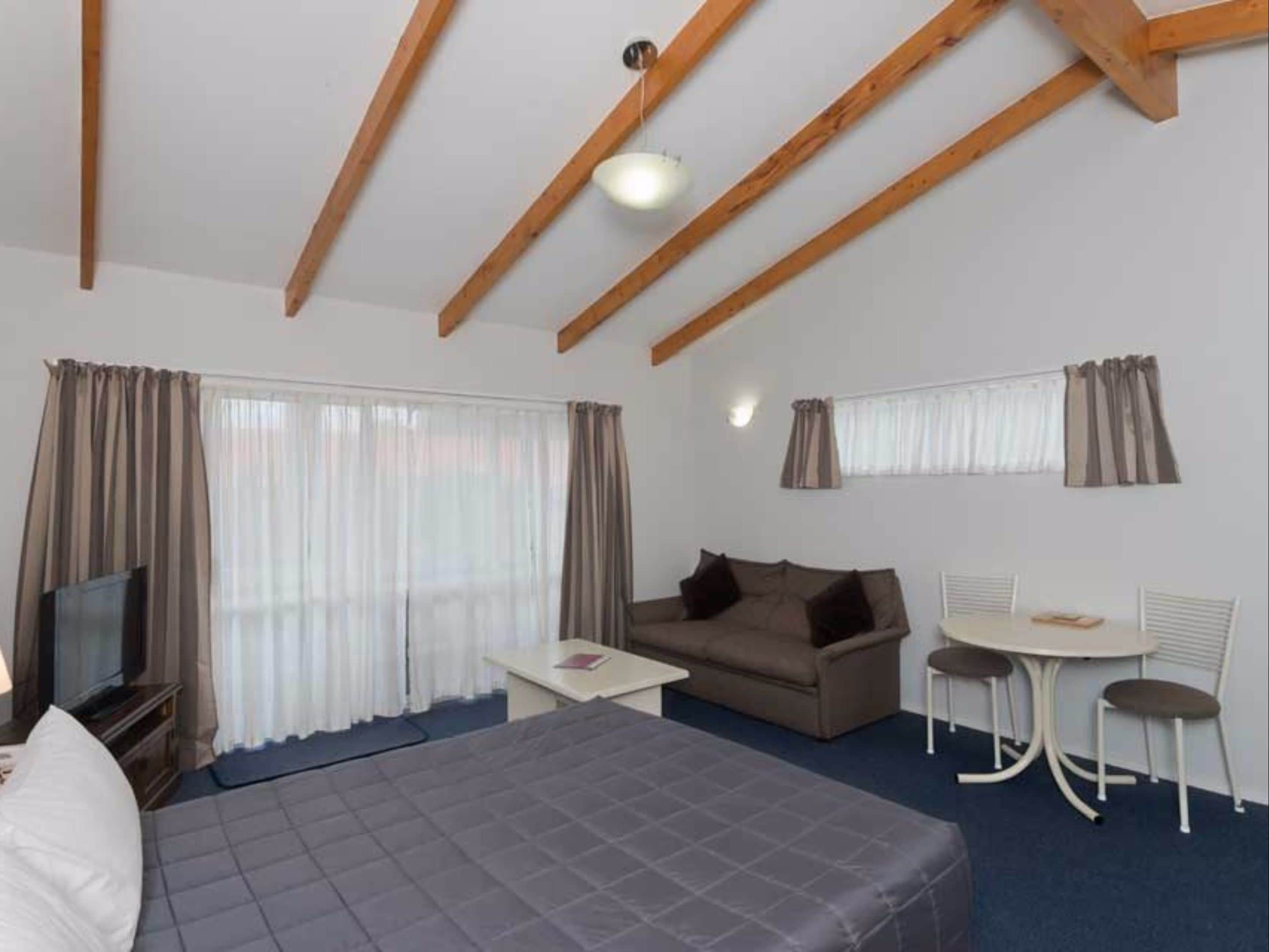 A room with a bed, a sofa, a small table, a TV, and a dining area with chairs.