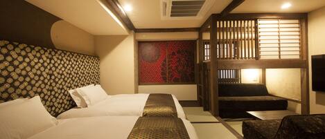 Una habitación de hotel al estilo japonés tradicional, con suelo de tatami, dos camas con ropa de cama estampada, un banco de madera bajo y una puerta corrediza con un diseño geométrico rojo.