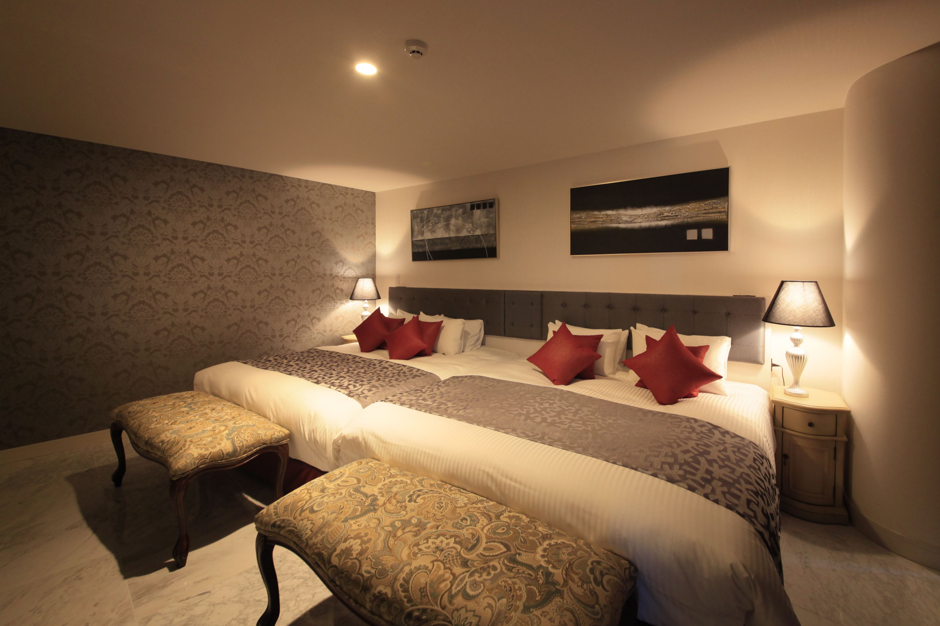 Een hotelkamer met een groot bed, twee nachtkastjes, een bankje en twee wandlampen.