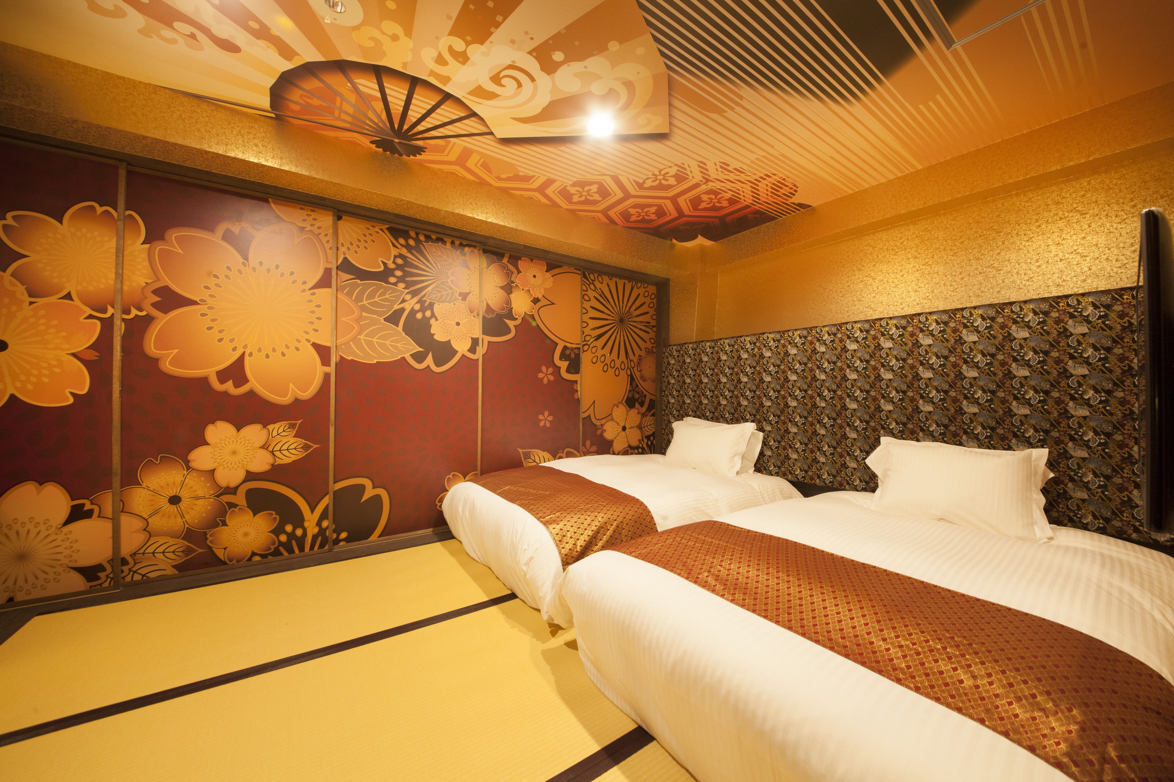 A hotel room with two beds, a decorative ceiling fan, and a patterned wall.