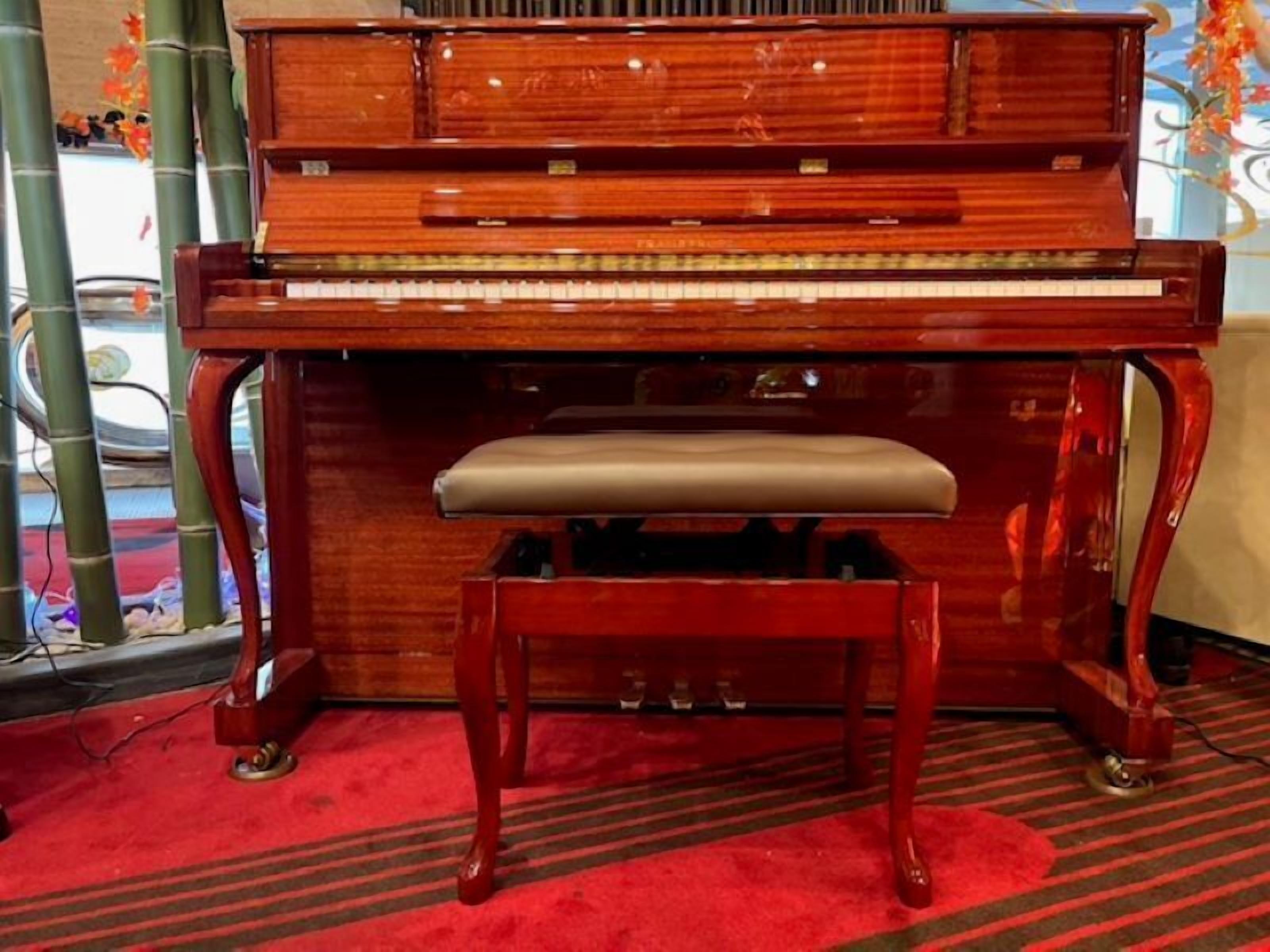 A grand piano with a bench in a room with a red carpet and bamboo decor.
