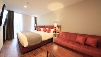 A hotel room with a large bed, a red sofa, a wooden coffee table, and a TV mounted on the wall.