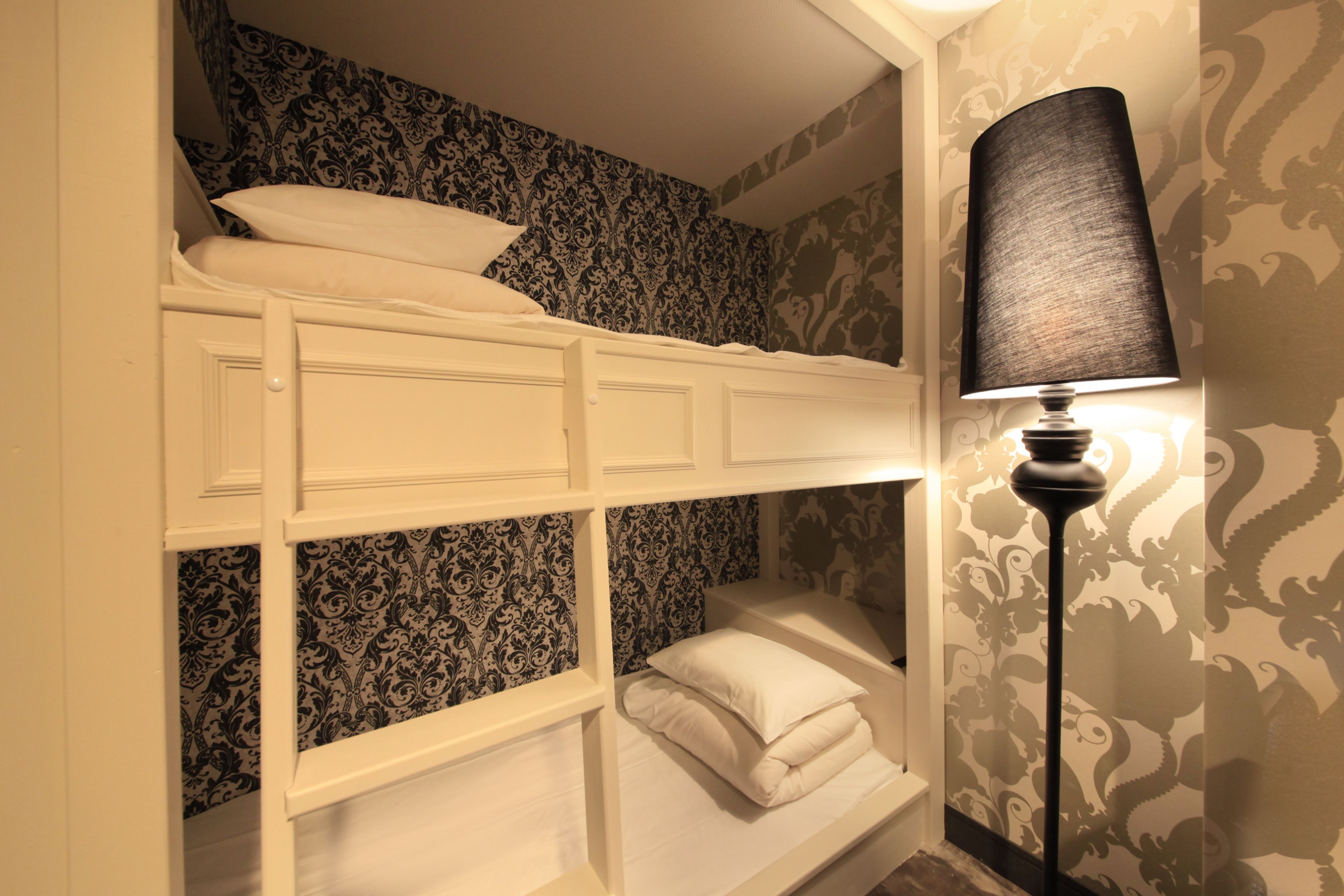 A bunk bed with white bedding and a black lamp beside it.