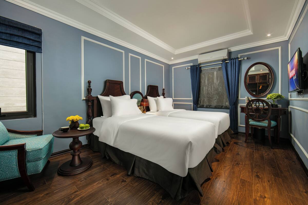 Habitación de hotel con cama doble, escritorio, silla, televisor y ventana con cortinas.