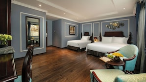 A hotel room with two beds, a sitting area with a chair, a small table with a vase and book, and a mirror on the wall. - Romantique Hotel De Hanoi (Hanoi)