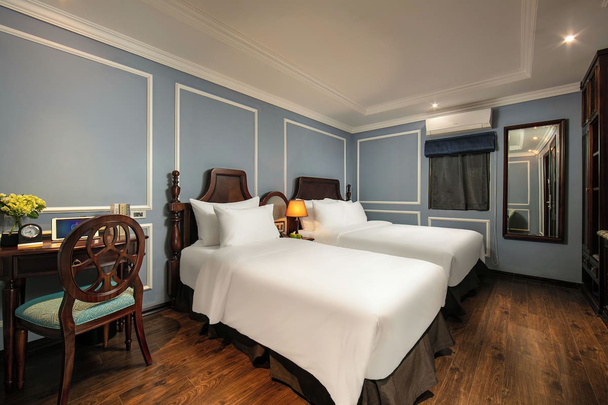 Habitación de hotel con dos camas, un escritorio con silla, una lámpara y un espejo grande.