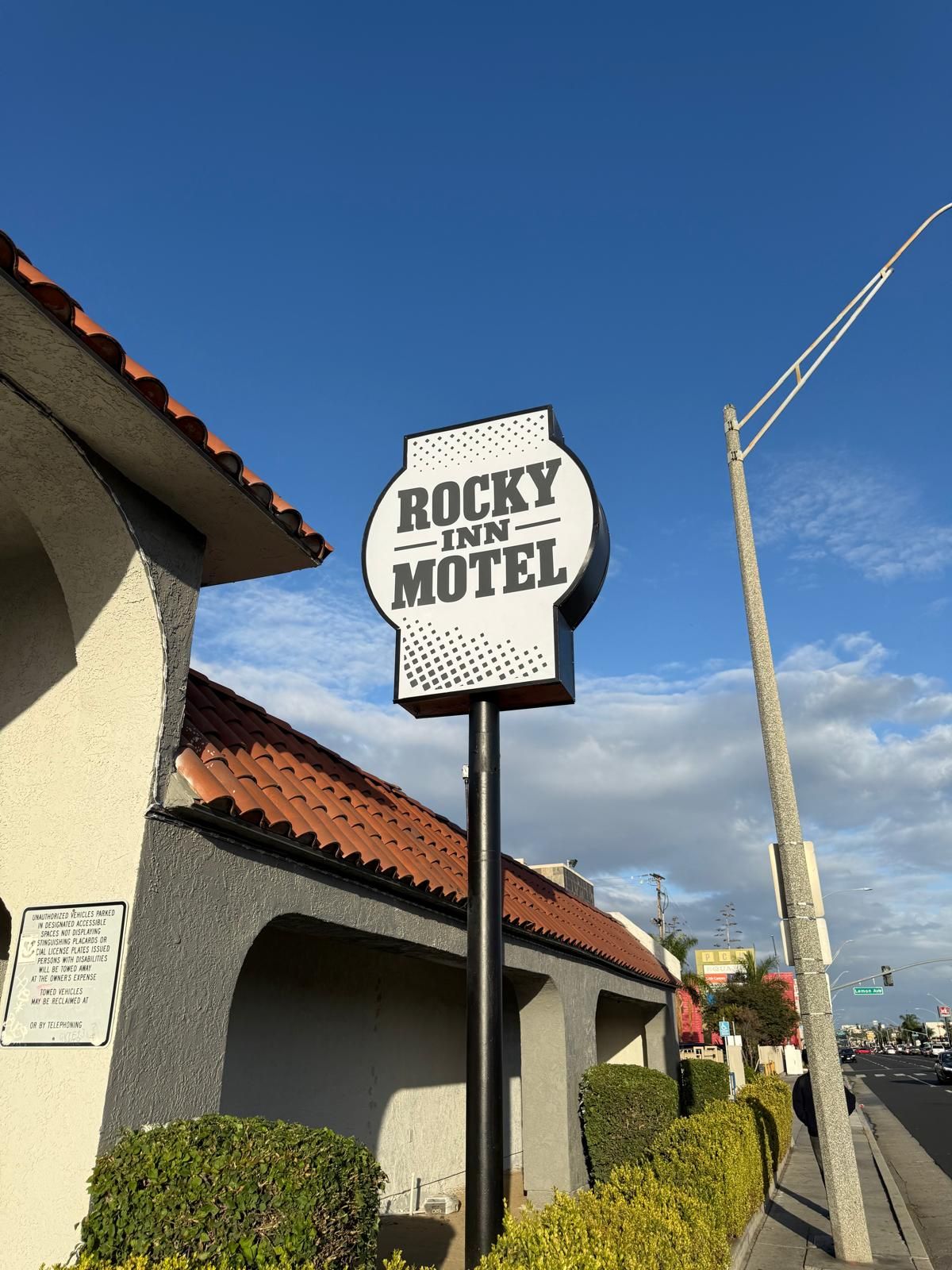 Señal de motel con el nombre 'ROCKY INN MOTEL' y una advertencia sobre vehículos no autorizados.
