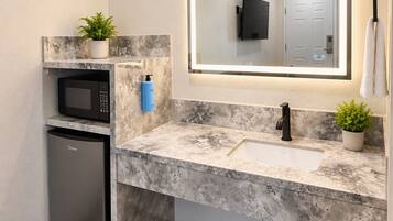 A modern bathroom with a marble countertop, a built-in sink, a microwave, and a small refrigerator.