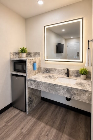 A modern bathroom with a marble countertop, a built-in sink, a microwave, and a small refrigerator. - Rocky Inn Motel (Long Beach)