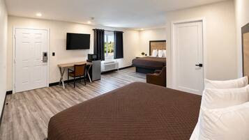 A hotel room with a large bed, a desk with a chair, a television, and a window with curtains.
