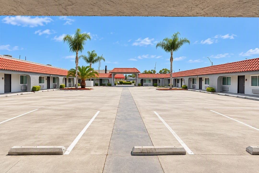 A motel with a central courtyard, individual rooms with red-tiled roofs, and palm trees.