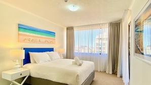 A hotel room with a bed, a nightstand, a wall art piece, and a window with curtains.