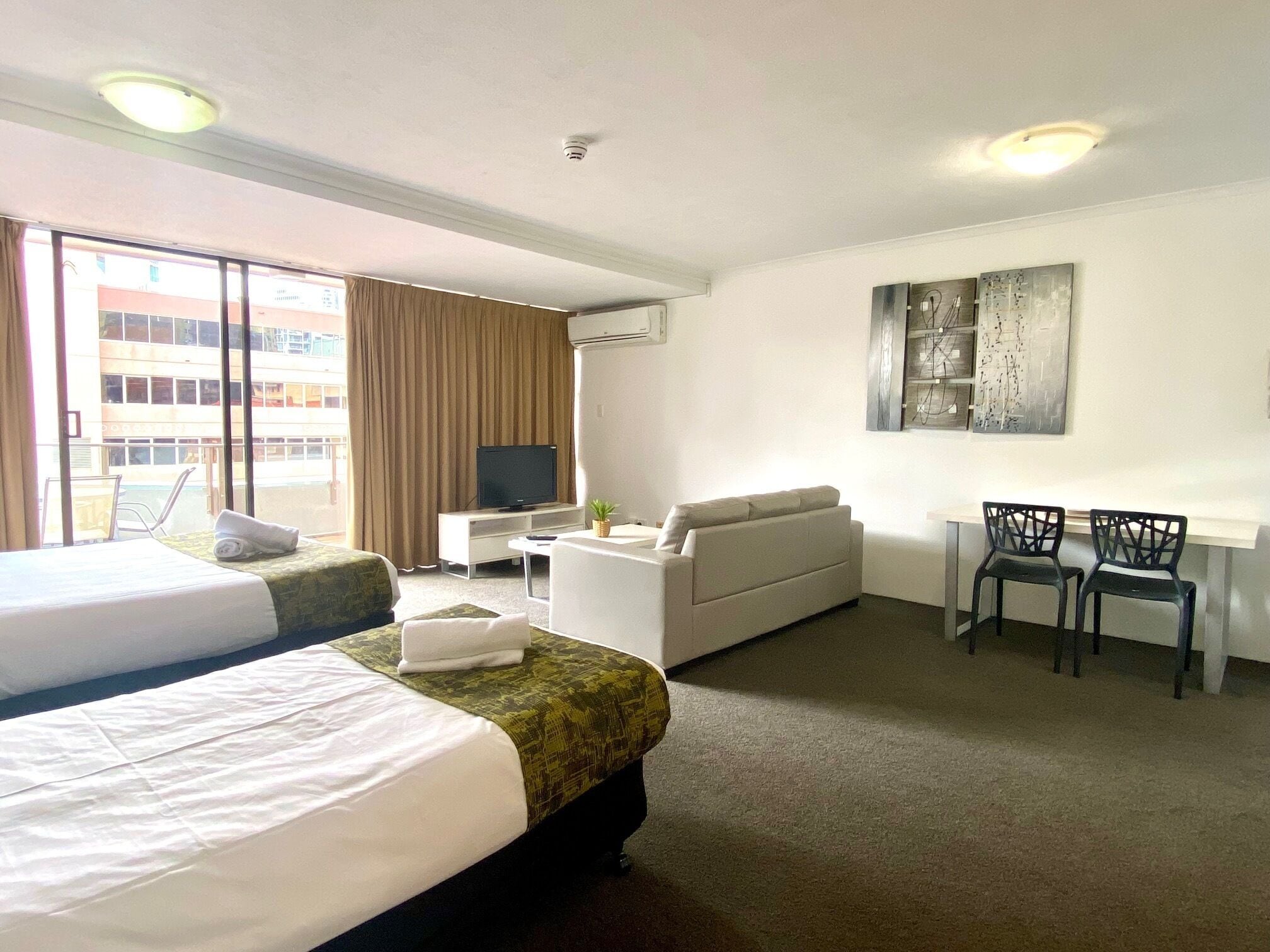 Ein Hotelzimmer mit zwei Betten, einem Schlafsofa, einem Fernseher, einem Schreibtisch mit Stühlen und einem Bild an der Wand.
