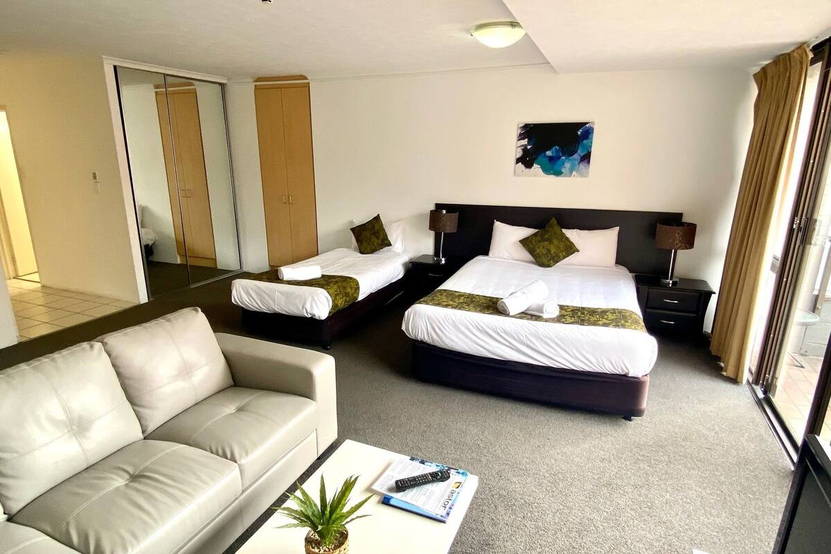 Una habitación de hotel con dos camas, un sofá, una mesita de centro y una pequeña planta.