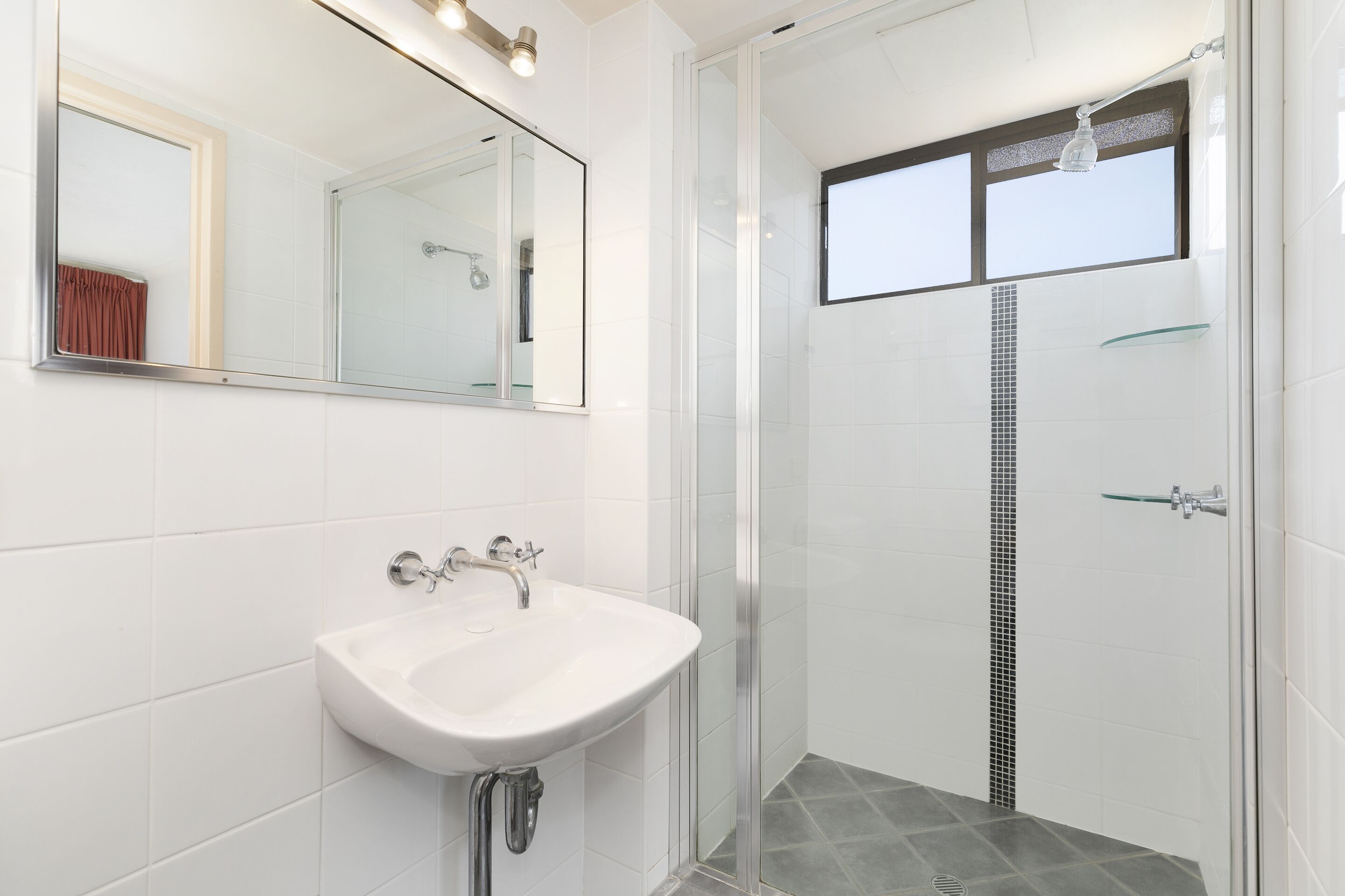 A modern bathroom with a white sink, a glass shower enclosure, and a large mirror.