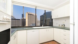 A modern kitchen with white cabinets, a dishwasher, and a window overlooking a cityscape.
