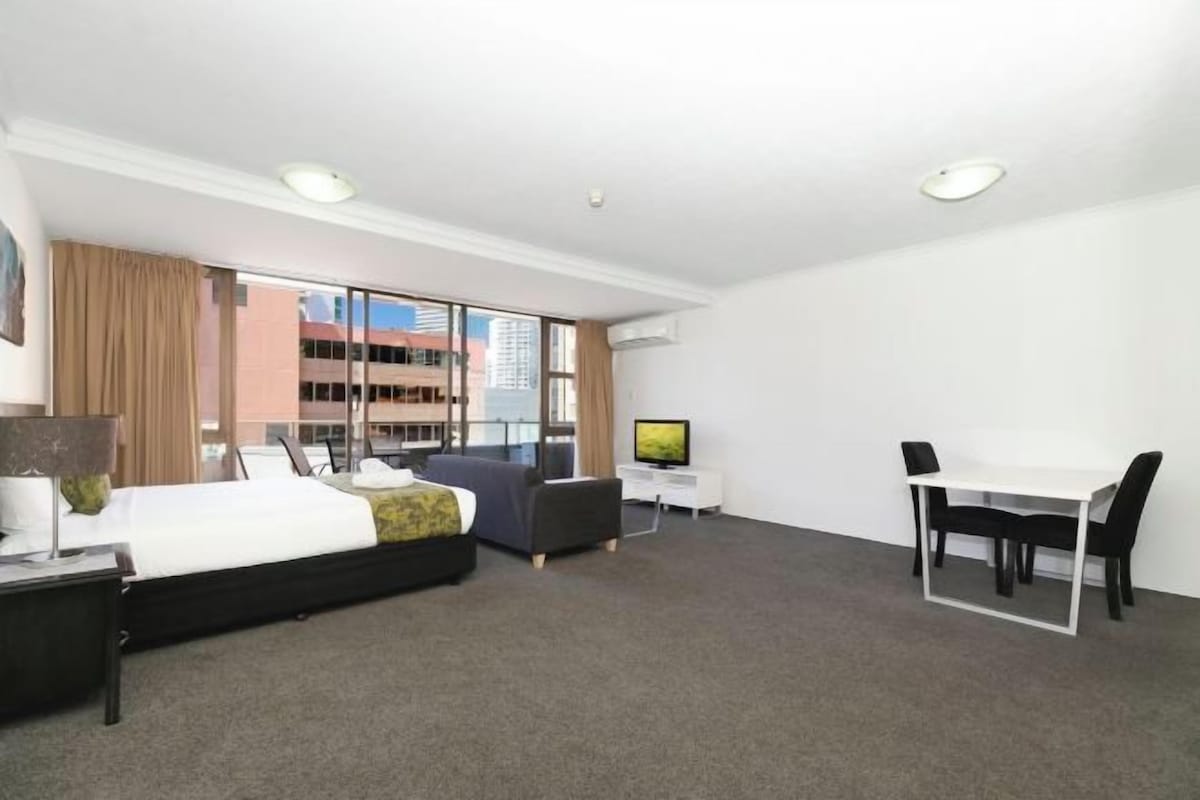 A modern hotel room with a bed, a desk, a chair, and a TV.