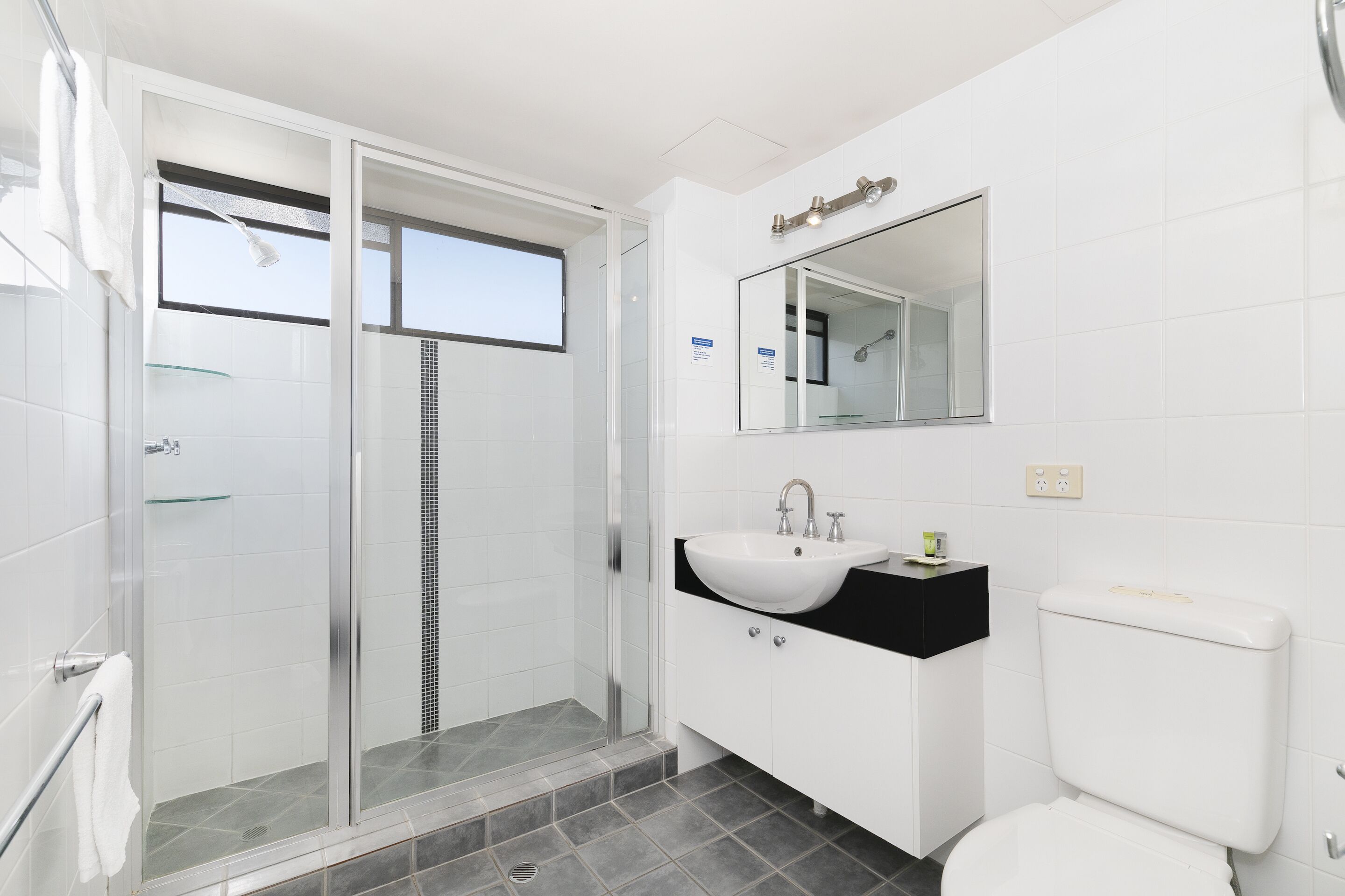 Un baño moderno con cabina de ducha de vidrio, un lavabo blanco y un inodoro.