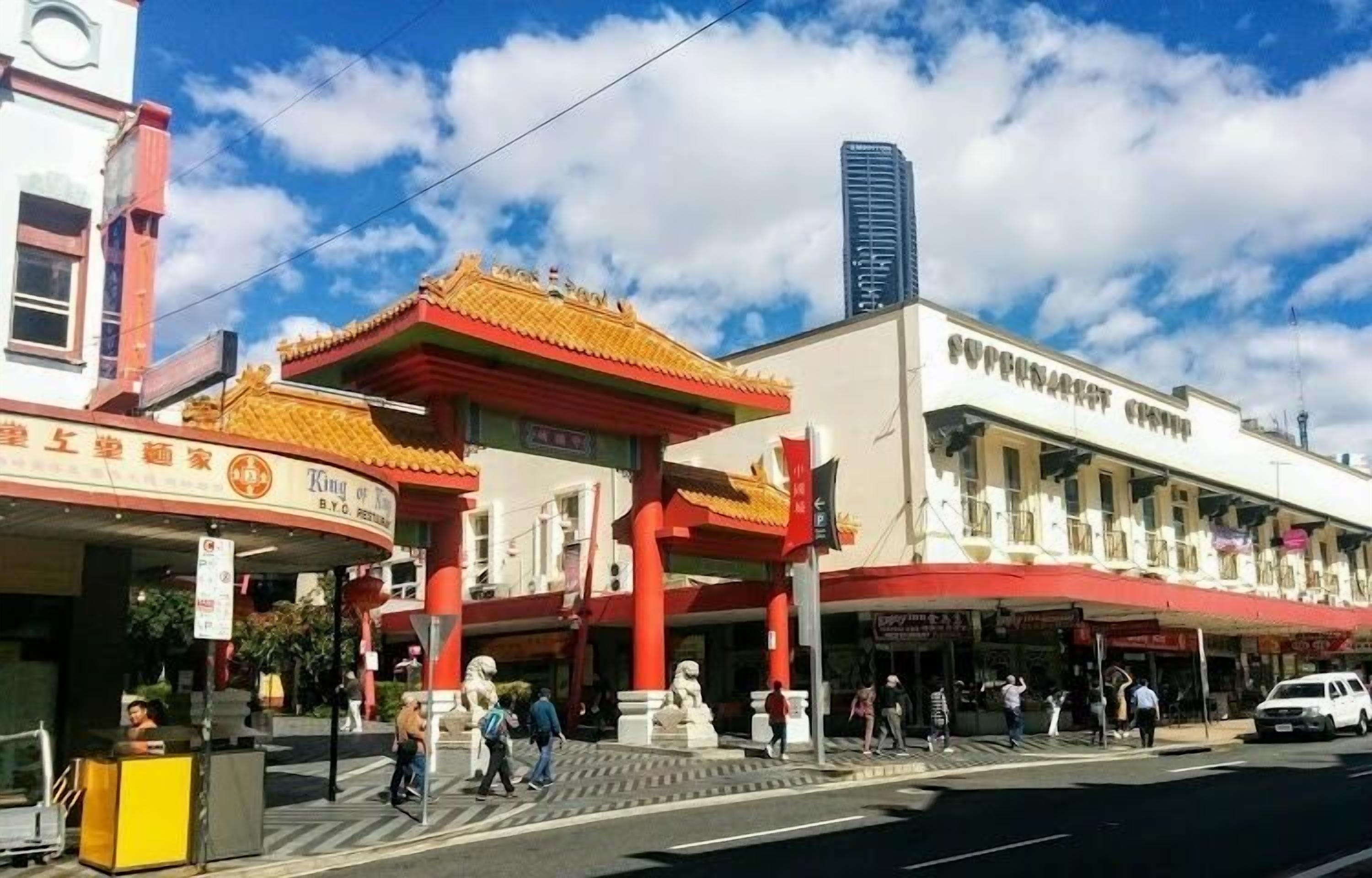 A traditional Chinese architectural building with a red roof and golden accents, adjacent to a modern white building with a sign that reads "SUPERMARKET".