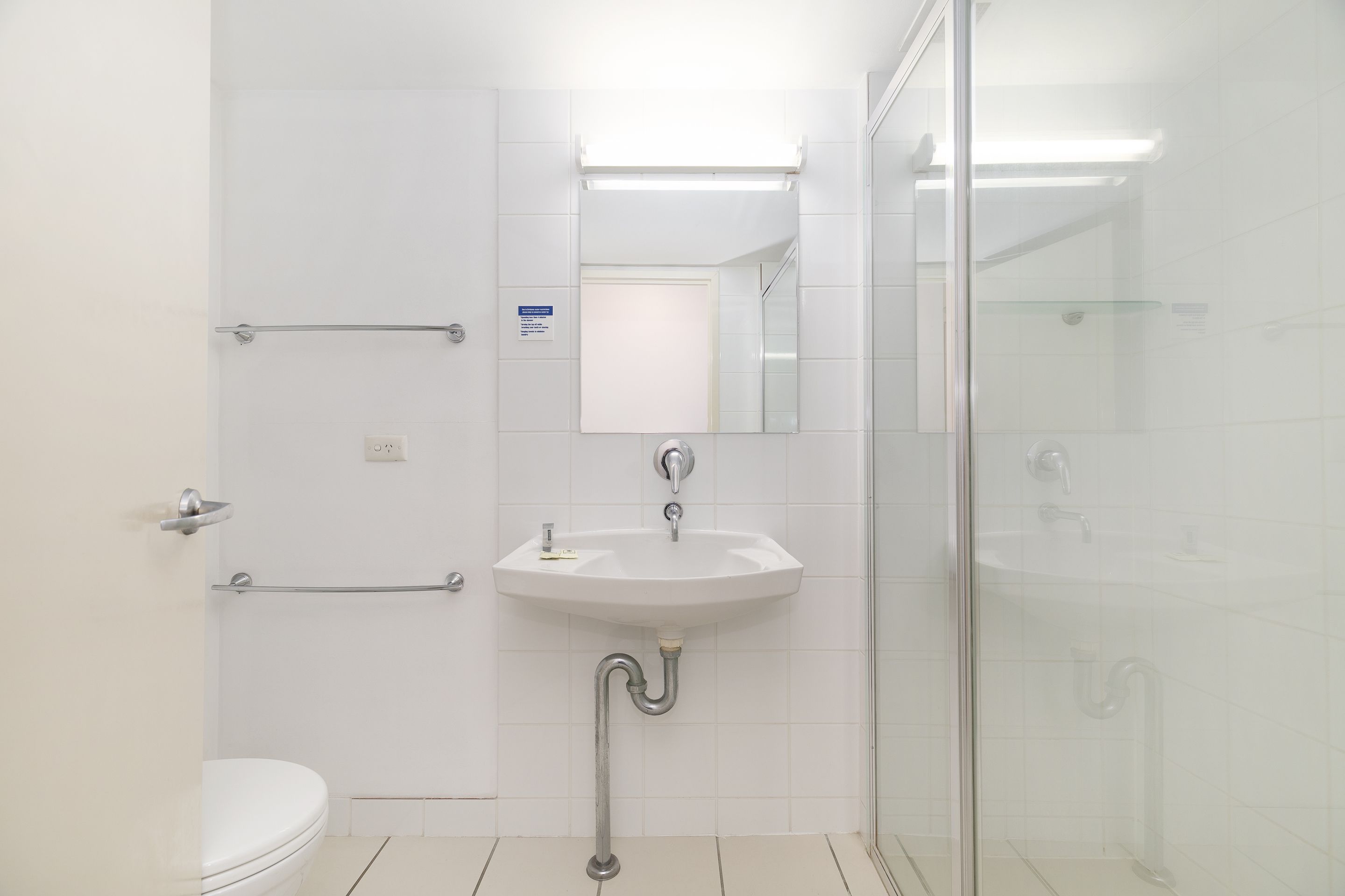 Une salle de bain moderne avec un lavabo blanc, un miroir et une cabine de douche en verre.
