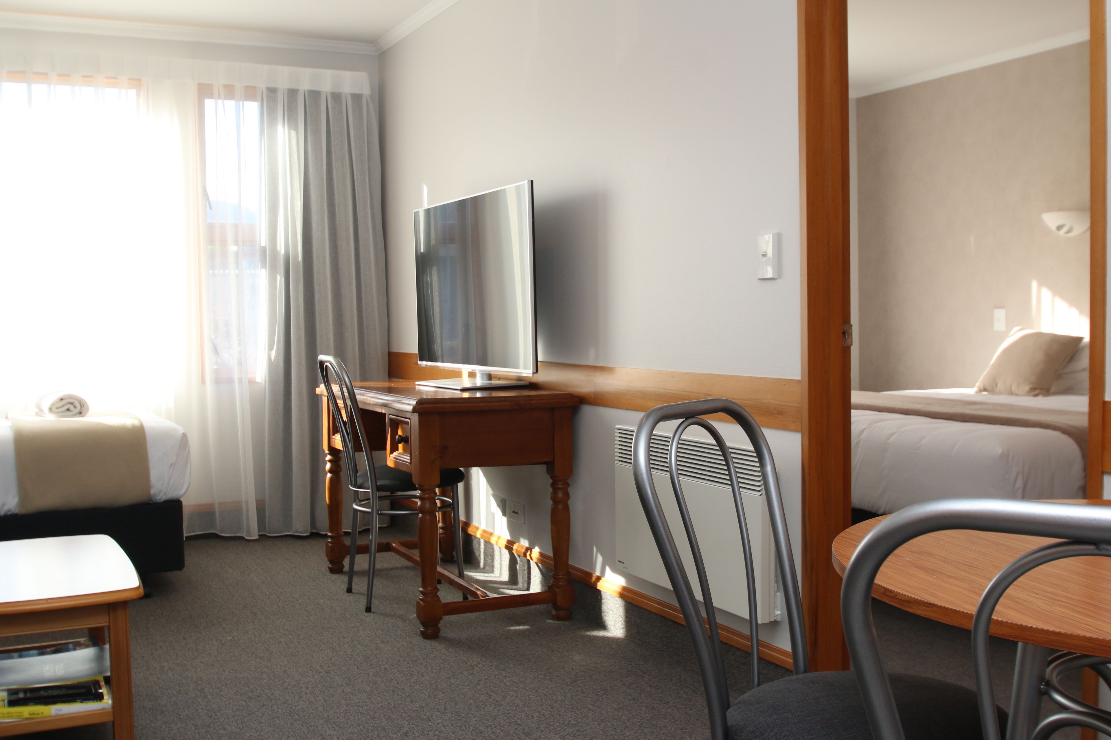 A hotel room with a bed, a desk with a chair, a television, and a window with curtains.