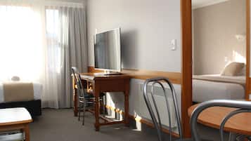 A hotel room with a bed, a desk with a chair, a television, and a window with curtains.