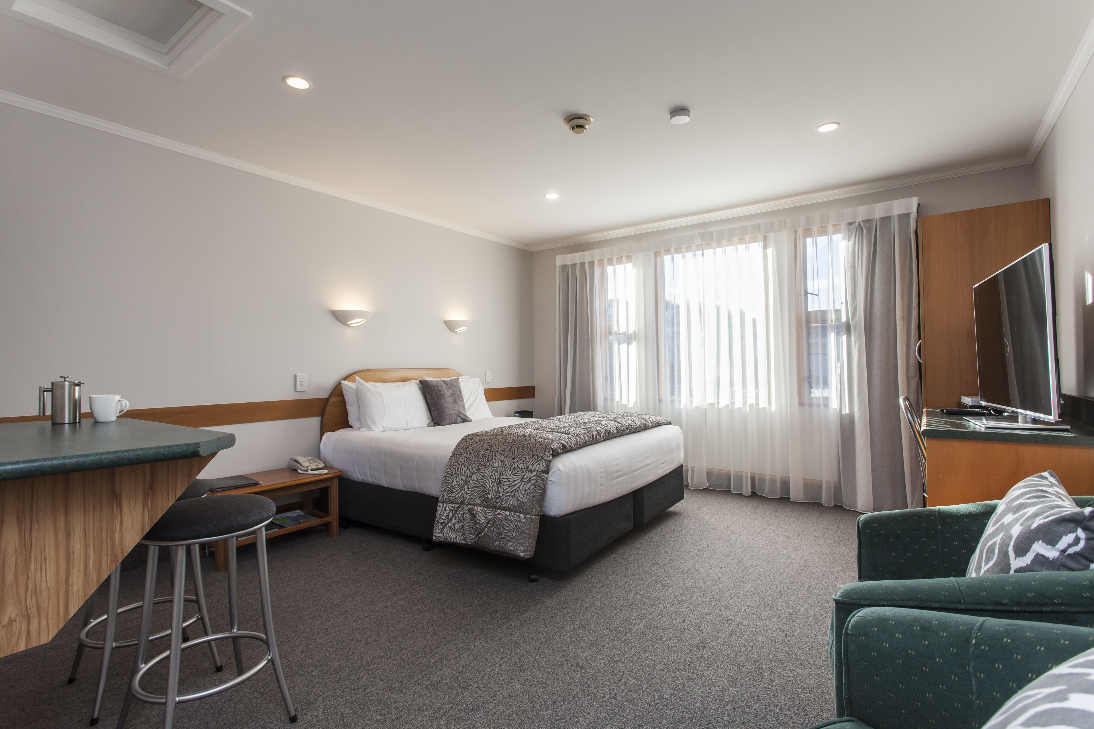 Habitación de hotel con cama, escritorio, silla, televisión y ventana con cortinas.