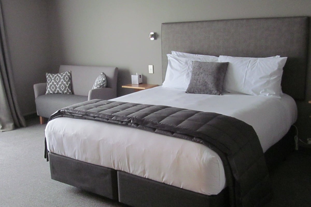 Una habitación de hotel con una cama grande, una mesita de noche, una silla y un sofá.