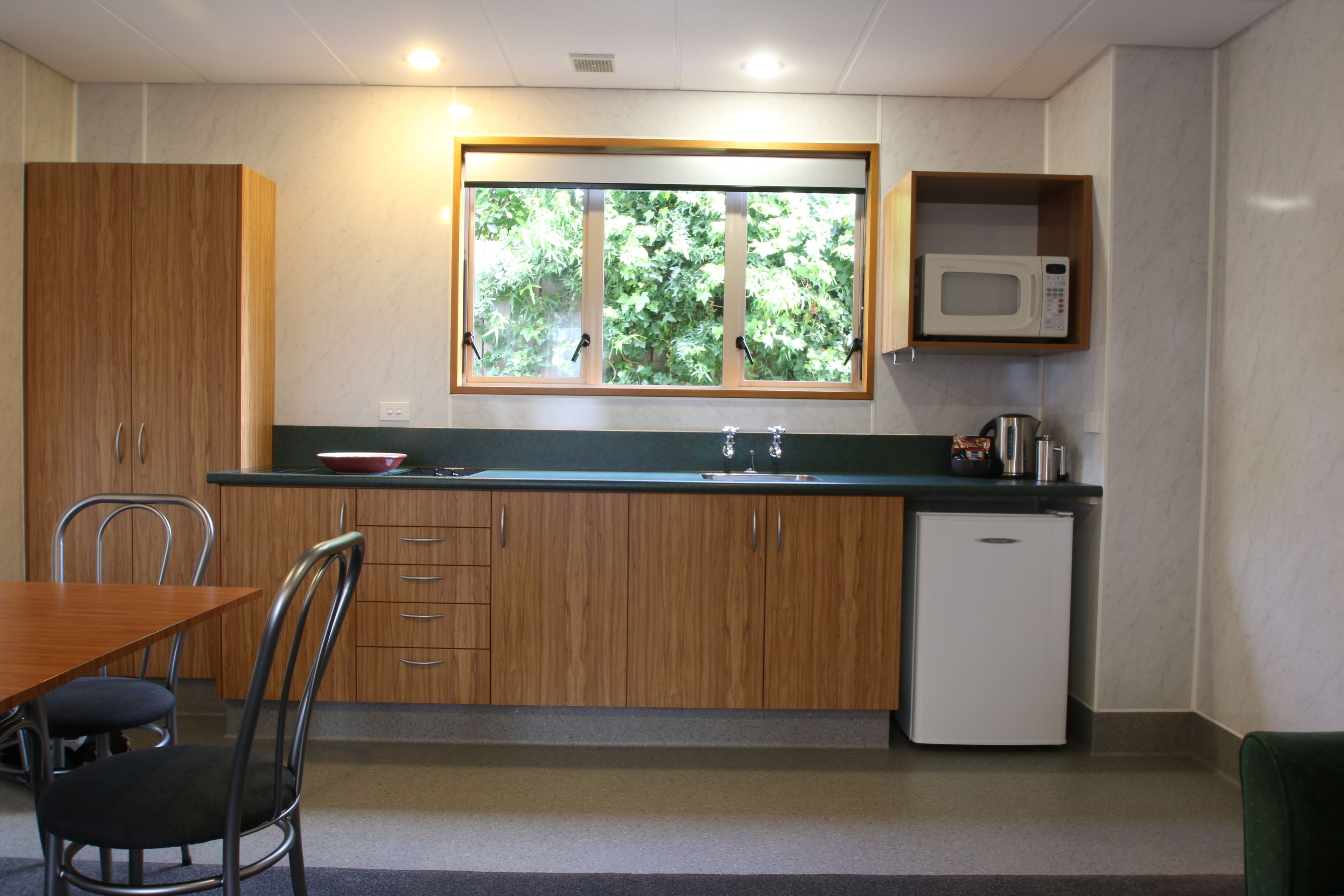 A compact kitchen with wooden cabinets, a built-in microwave, a sink, and a window with a view of greenery.