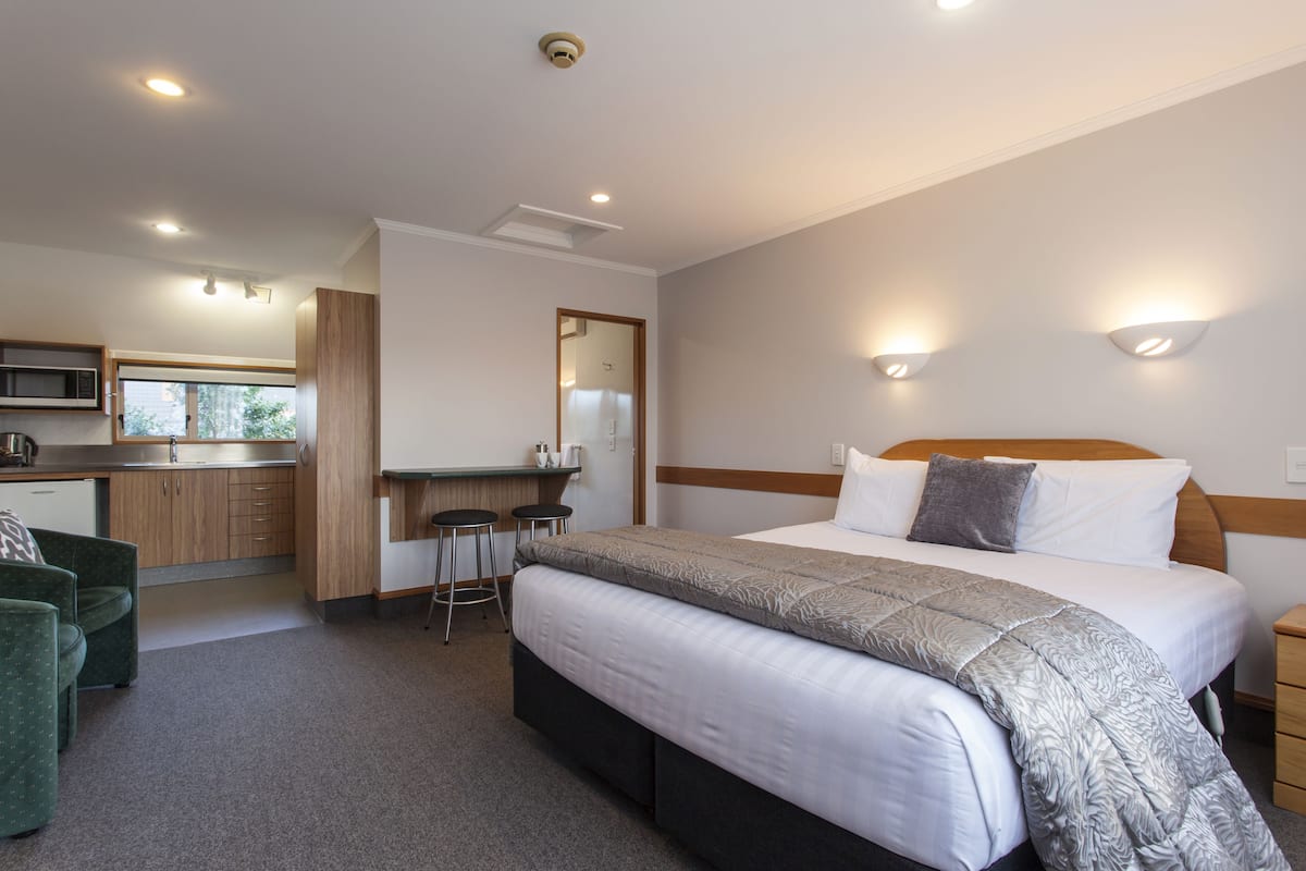 Habitación de hotel con cama, mesita de noche y una zona de kitchenette.