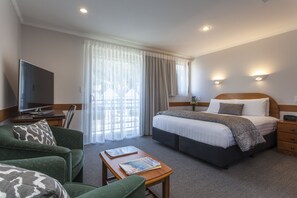 Habitación de hotel con cama, escritorio, silla, televisor y ventana con cortinas.