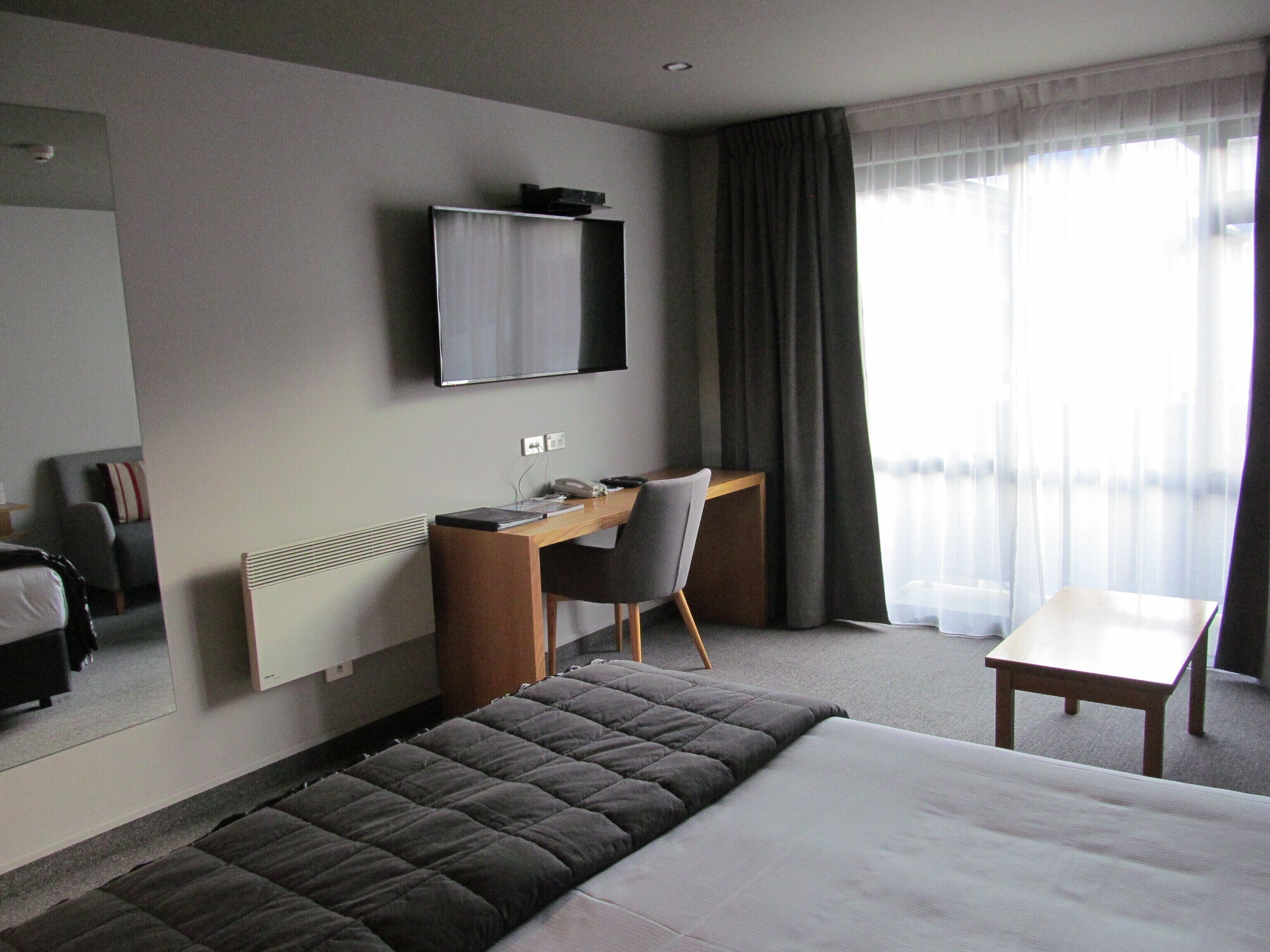 Habitación de hotel con cama, escritorio, silla, televisión y ventana con cortinas.