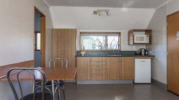 A compact kitchen with a wooden table and chairs, a built-in microwave, and a small refrigerator.