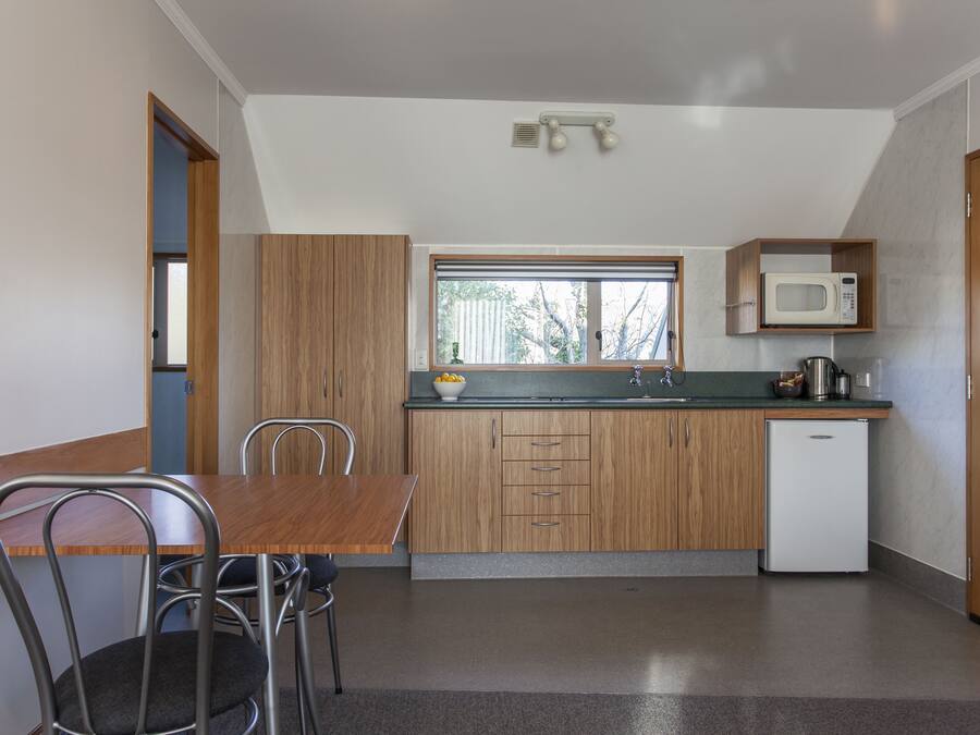A compact kitchen with a wooden table and chairs, a built-in microwave, and a small refrigerator.