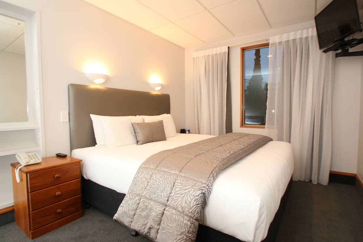 Habitación de hotel con una cama grande, lámparas de noche, mesita de noche, teléfono y televisión en la pared.