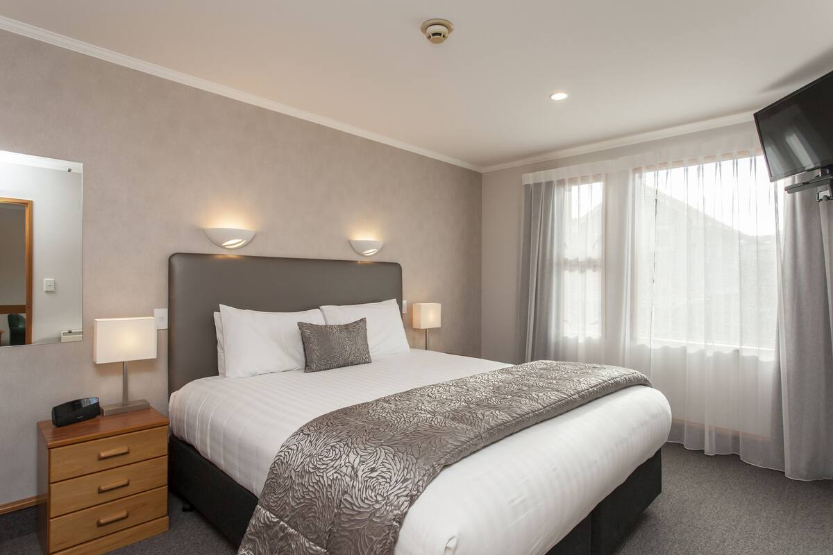 Una habitación de hotel con una cama grande, dos lámparas de noche, un televisor de pantalla plana, una mesita de noche y un espejo.