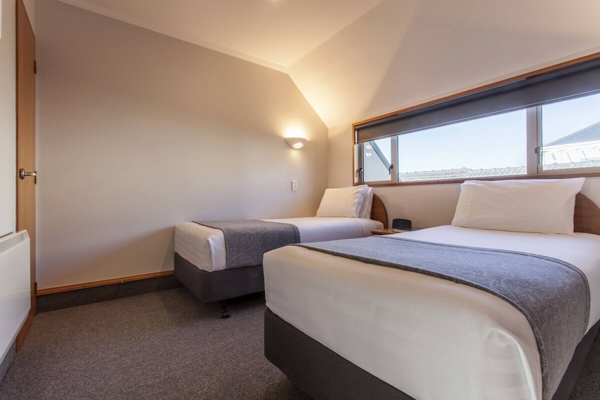 Habitación de hotel con dos camas, ventana con vistas y una lámpara de pared.