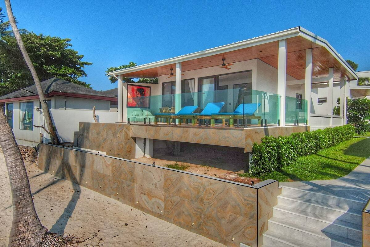 Una casa moderna frente a la playa, con balcón de cristal, piscina y vista al océano.
