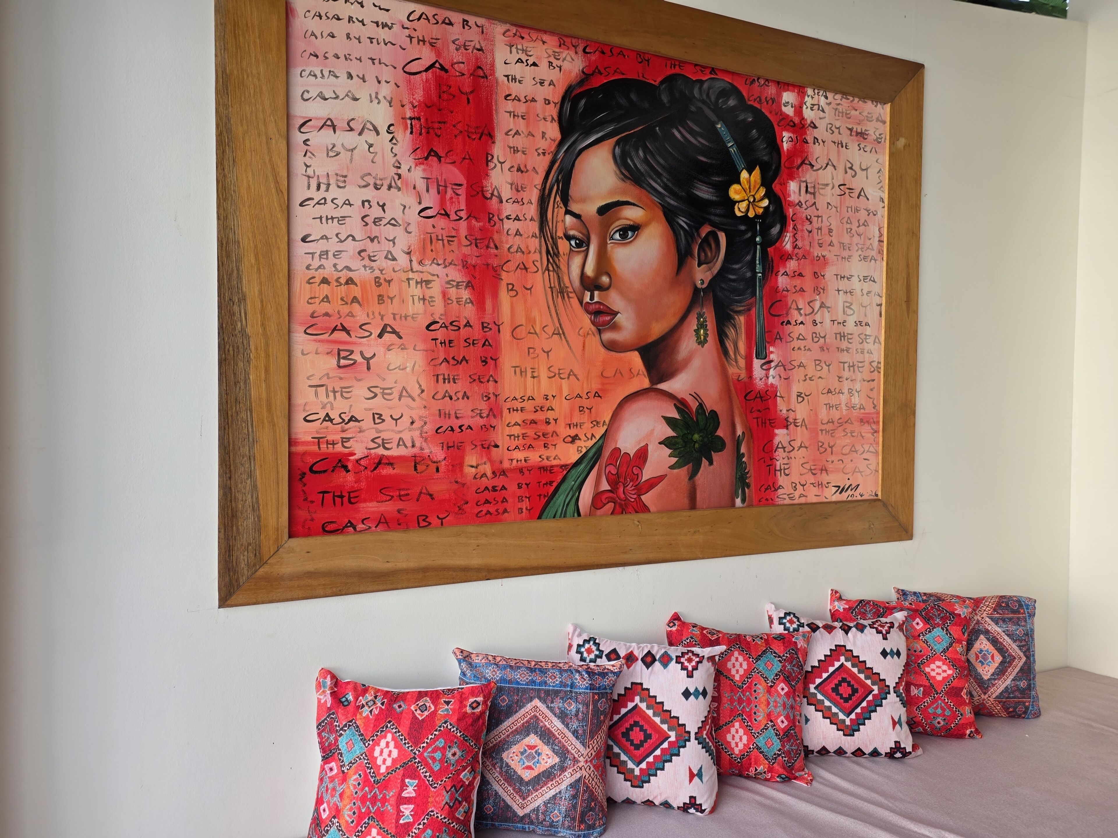 Una obra de arte enmarcada con el texto repetido 'CASA BY THE SEA' en una pared, junto con una serie de cojines estampados.