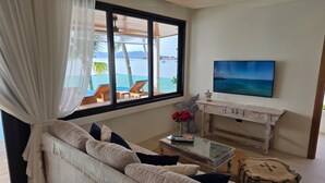 Uma sala de estar com sofá, mesa de centro, televisão e vista para o mar.