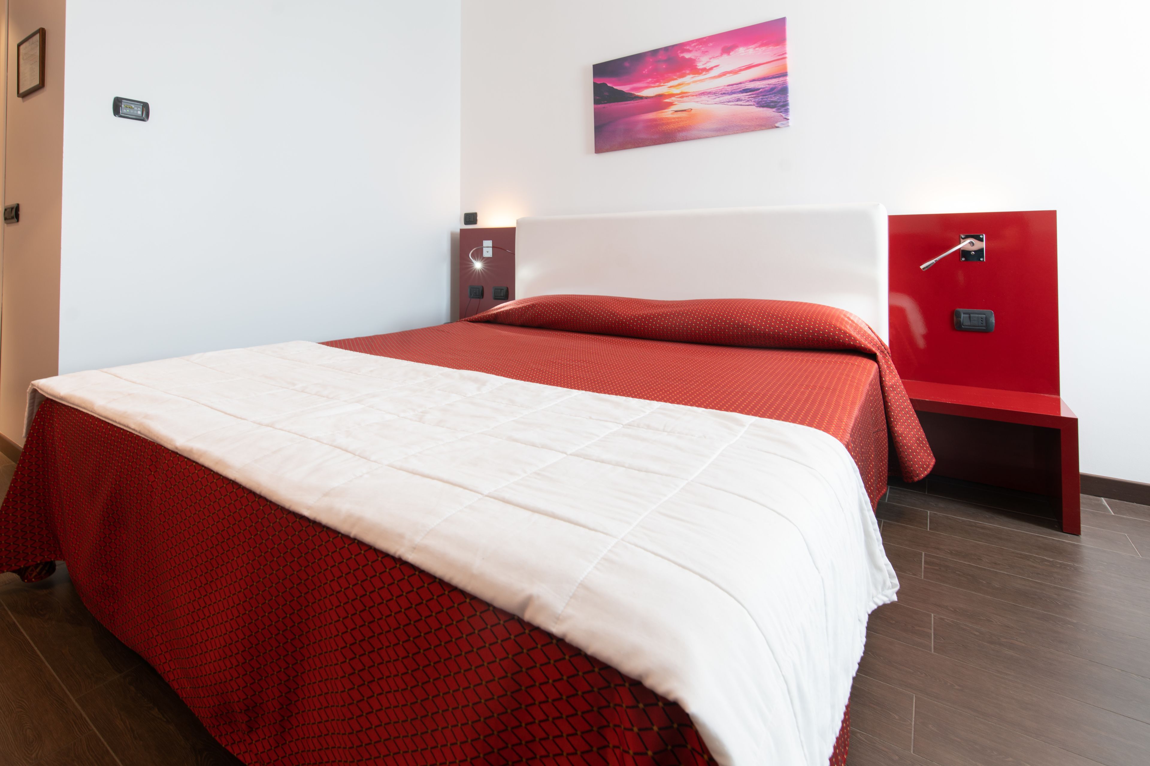 Una cama bien hecha con una colcha roja y blanca, un cabecero rojo y una mesita de noche roja con una lámpara.
