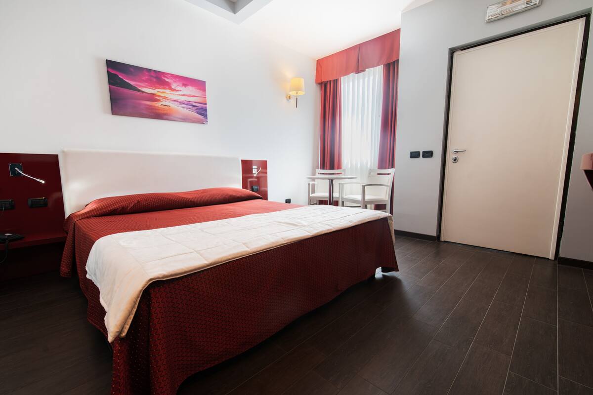 Habitación de hotel con una cama grande, un escritorio, una silla, una mesita, un cuadro y una puerta.