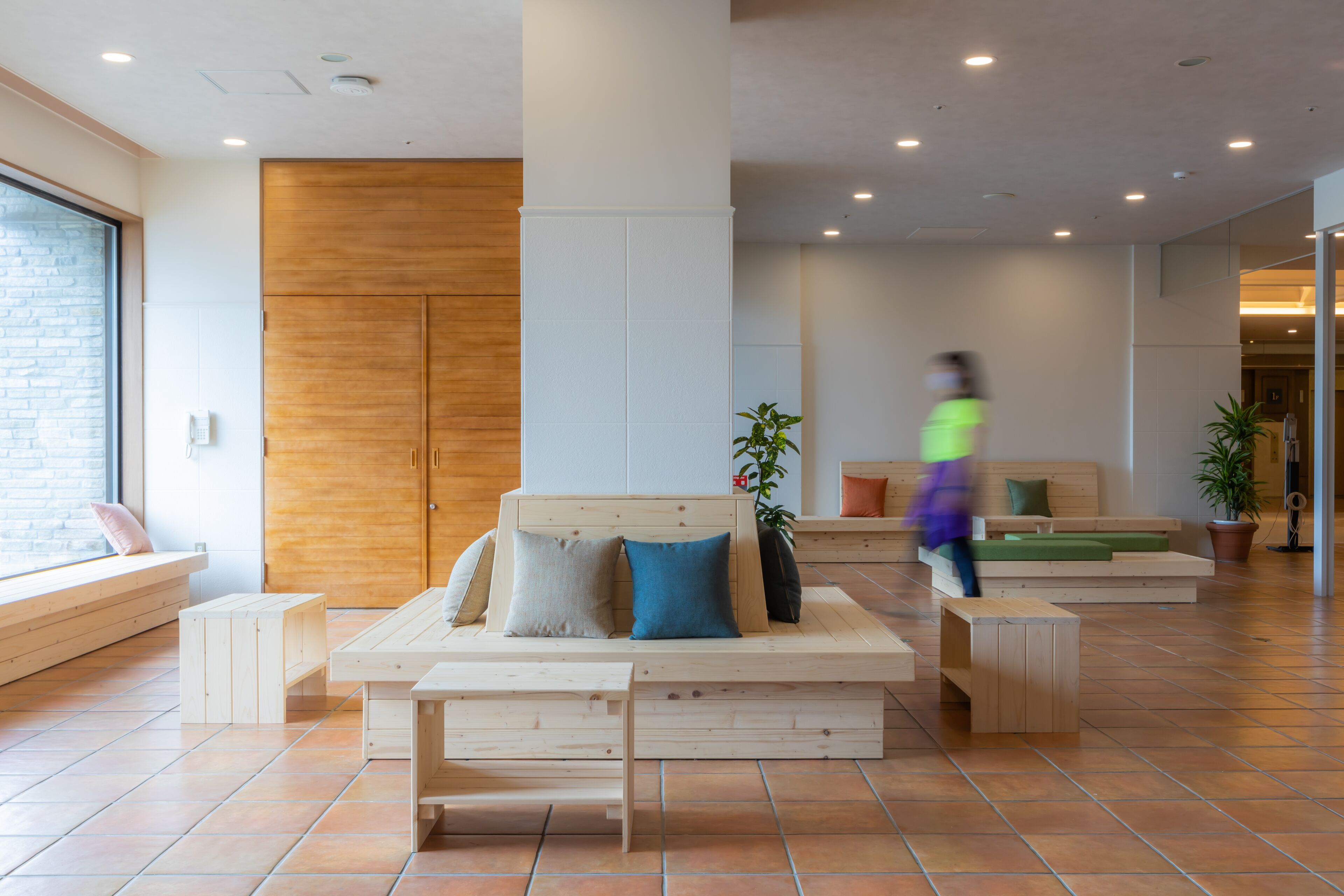 A modern lobby with a wooden sofa, benches, and potted plants.