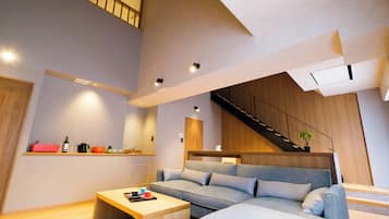 A modern living room with a grey sectional sofa, wooden coffee table, and a staircase leading to an upper level.
