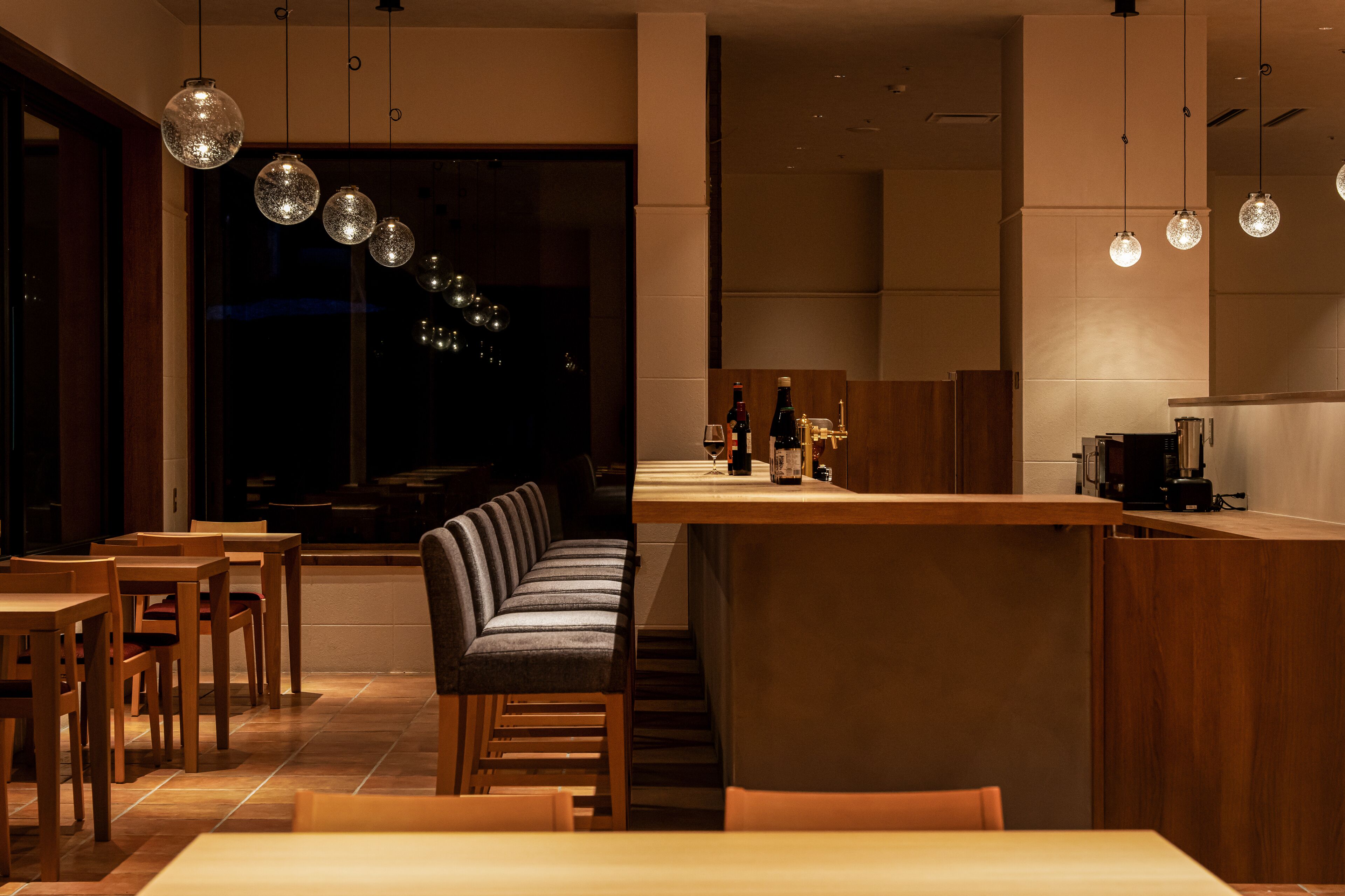 A modern restaurant with wooden furniture, a bar area, and pendant lighting.